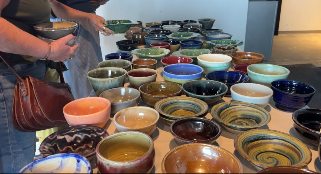 Event goers grab bowls from a table full of colorful dishes.