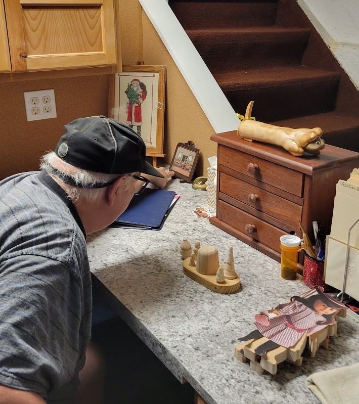 Gary Steffen sitting at his marble desk presenting projects he made, including wooden toys and paintings.