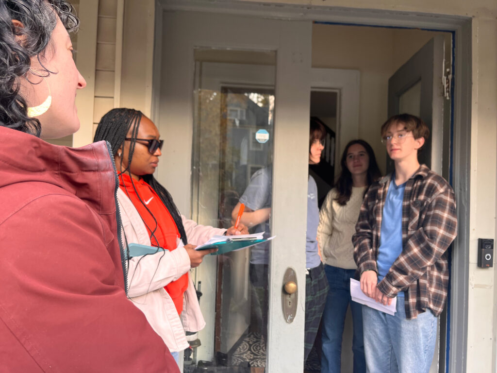 Valerie Baron of the NRDC and Kiara Van Brackle of Syracuse University stand at the door with three residents of an impacted home.