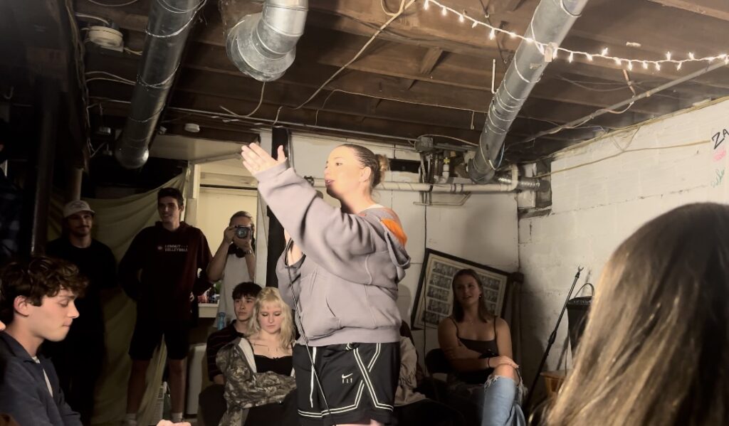 Liz Crandall performing, talking to an audience member. She's in the audience, and someone is off stage photographing her.