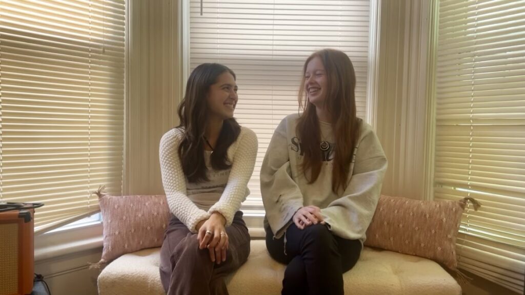 Two girls sit in a bay window and talk to each other.