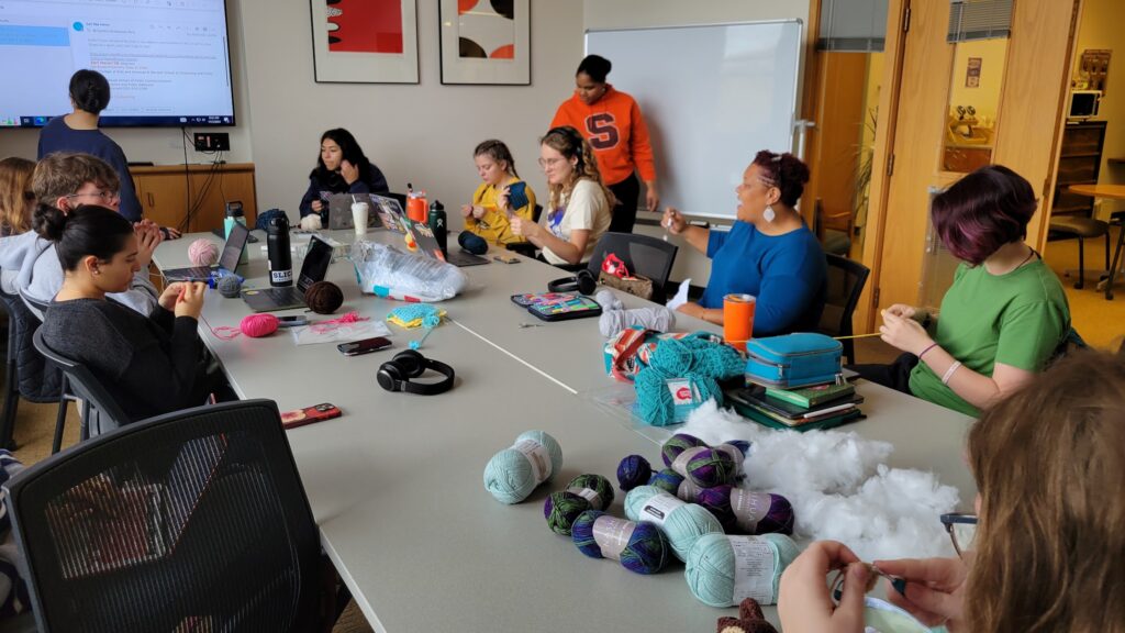 Students sitting around a long table crocheting and listening to their instructor, Syeisha Byrd.