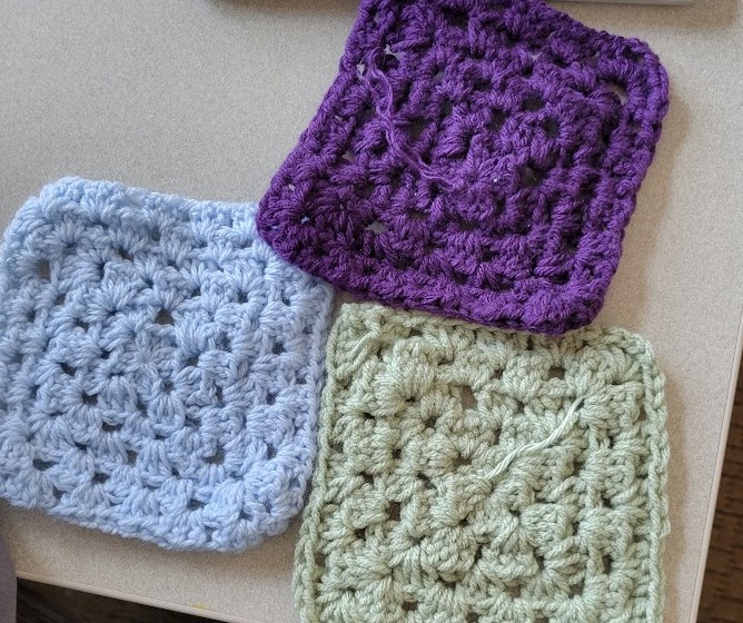 Three crocheted granny squares laid out on a table.