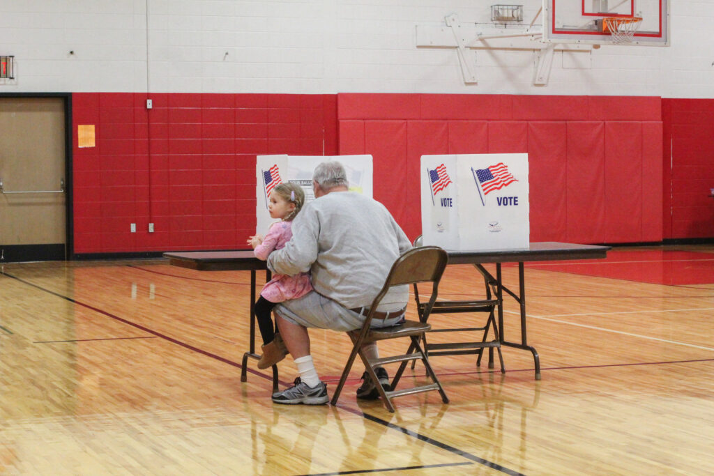 A man and his granddaughter sit together as he fills out a ballot at Blessed Sacrament School in Syracuse, NY on November 5, 2024. Participating in the democratic process and voting not only bring implications to the current generation but for those to come.