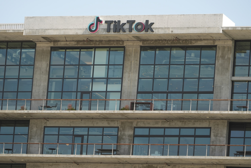 A TikTok sign sits against a beige building and above large windows. 