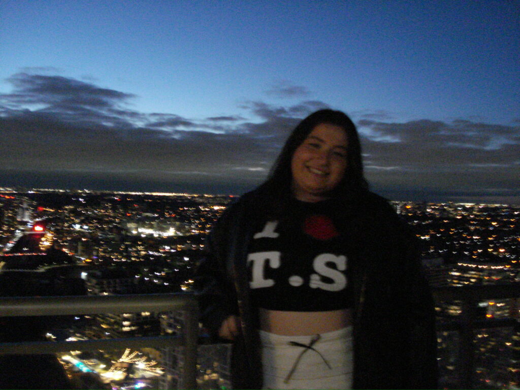 One girl stands on a balcony at night in Toronto wearing an I heart T.S. shirt. 