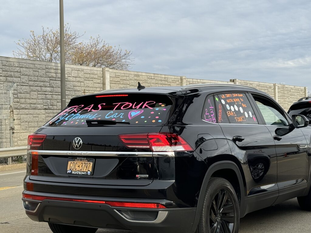 A car on the highway is painted saying "Eras Tour Getaway Car" with friendship bracelet beads. 