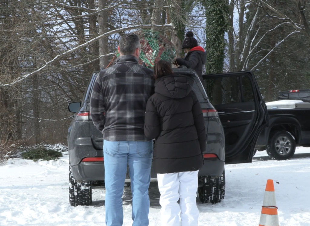 Father and daughter look as a member of Page's Christmas Tree farm helps them put their Christmas tree on the car.