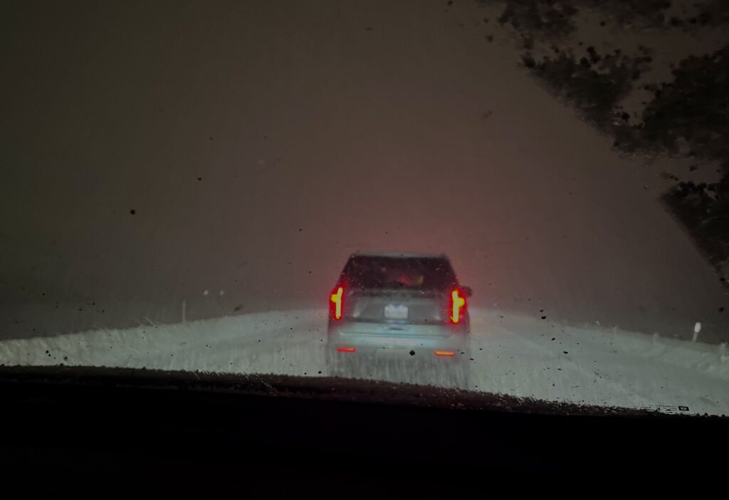 A snowy, icy road at night with a car up ahead.