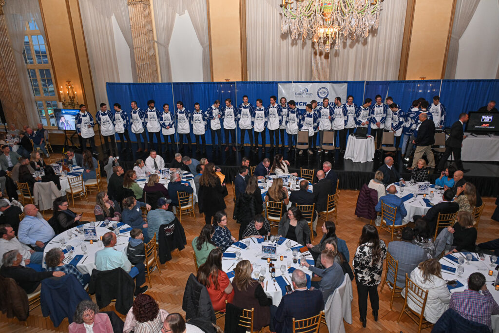 Hockey Players line up on a stage while people are sitting at tables.