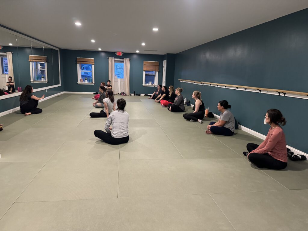 Participants engage in a self-defense class, listening attentively to their instructor in a welcoming studio space.