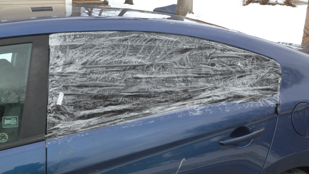 The back window of a blue Hyundai car, covered with tape and a trash bag to keep the elements out of the back seat.