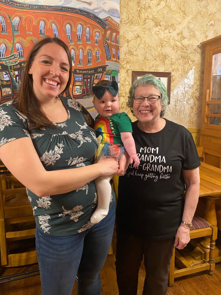 Brianna, a childhood cancer survivor, holds her daughter while her grandmother, Sue, continues her tradition of shaving her head every year at Kitty Hoyne's