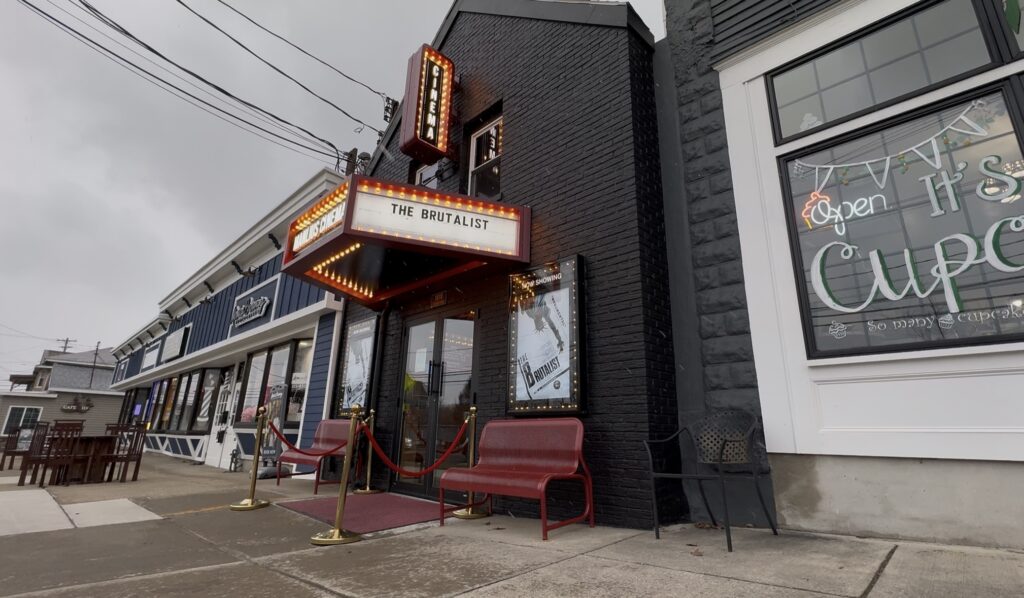 The outside of Manlius Cinema, with the lights illuminating the marquee. A red carpet and rope lead to the entrance, surrounded by two red benches