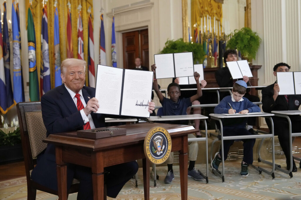 President Donald Trump holds up a signed executive order as young people hold up copies of the executive order they signed at an education event in the East Room of the White House.