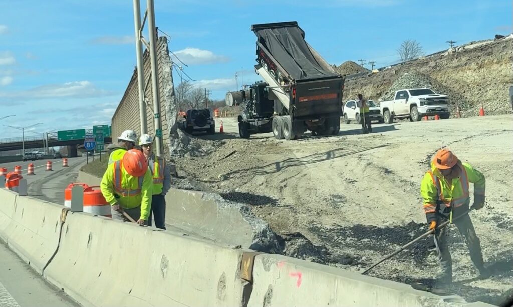 Construction workers spreading material on an I-81 highway shoulder.