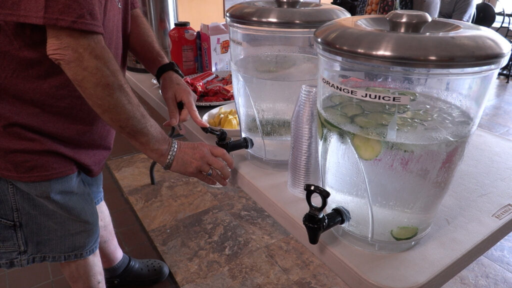 Two water stations next to each other as a man fills his cup at the one to the left. One container has just water, and the other has water and cucumber.