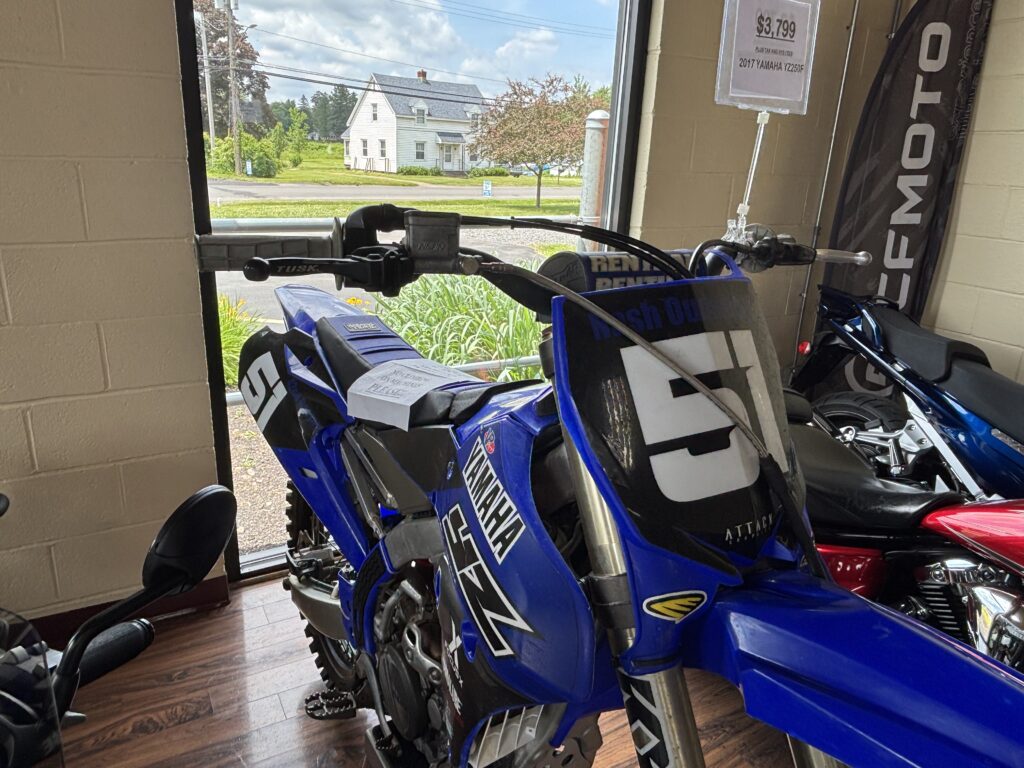 A royal blue dirt bike in a store in front of a window.