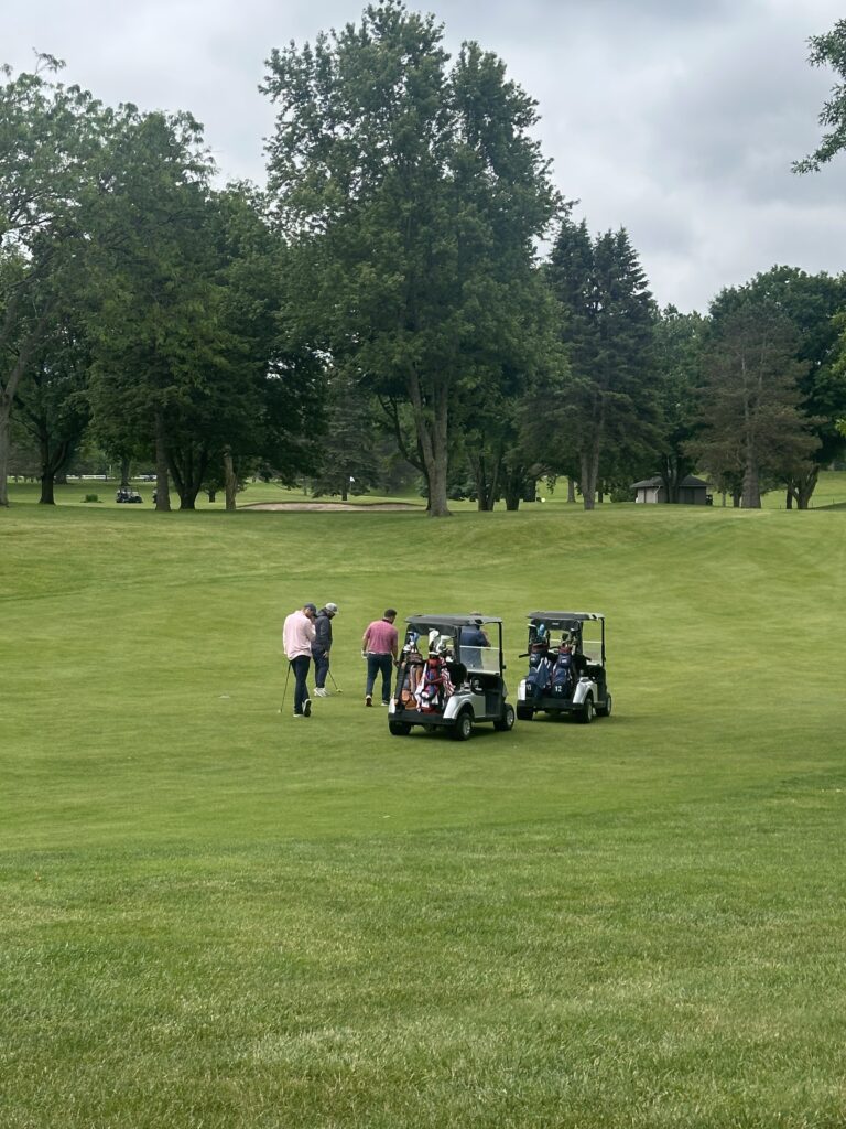 A group of male golfers out on the golf course with their gold carts.