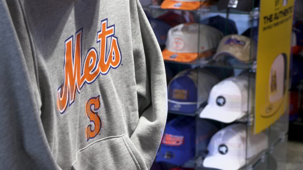 A Syracuse Mets sweatshirt hangs next to a shelf of hats.