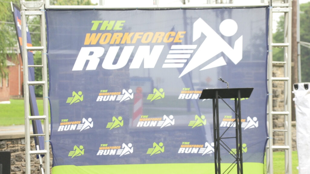 A large blue, fabric backdrop that reads "The Workforce Run".