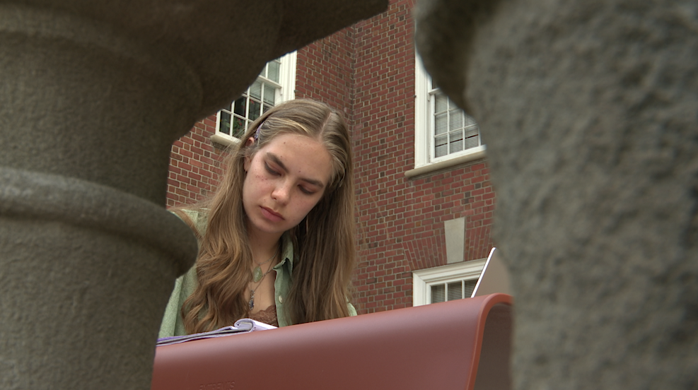 Student studying by the Maxwell School building 