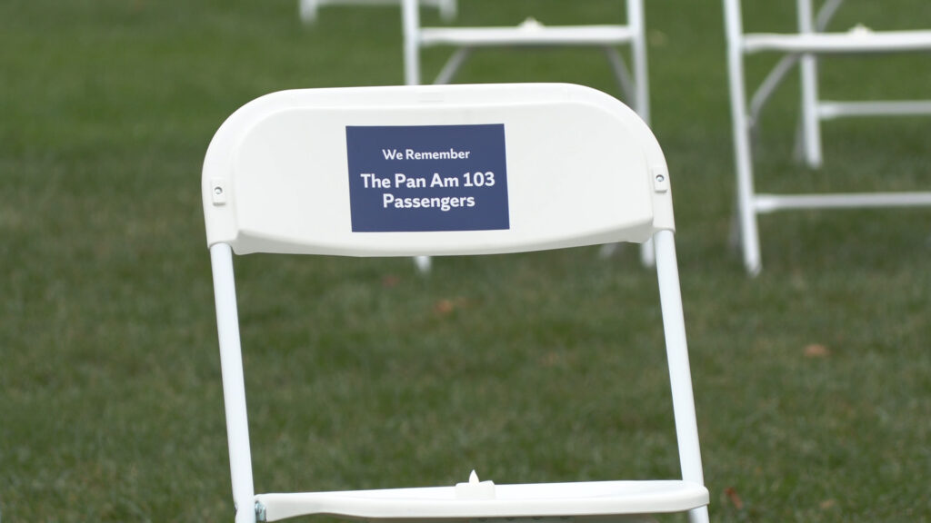 A picture of a white chair with a blue sticker on it reading "We Remember The Pan Am 103 Passengers"