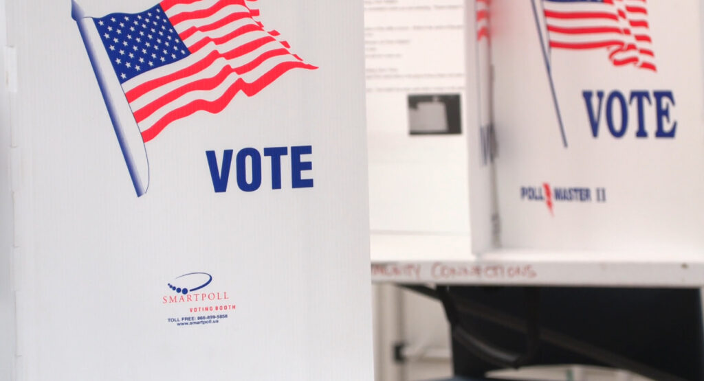 Voting booths display the word “Vote” with American flags at an Onondaga County polling site during early voting.