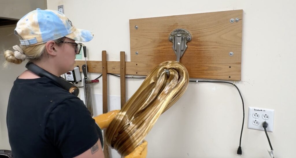 Current image: Hercules Candy Employee Making candy by pulling it on a hook.