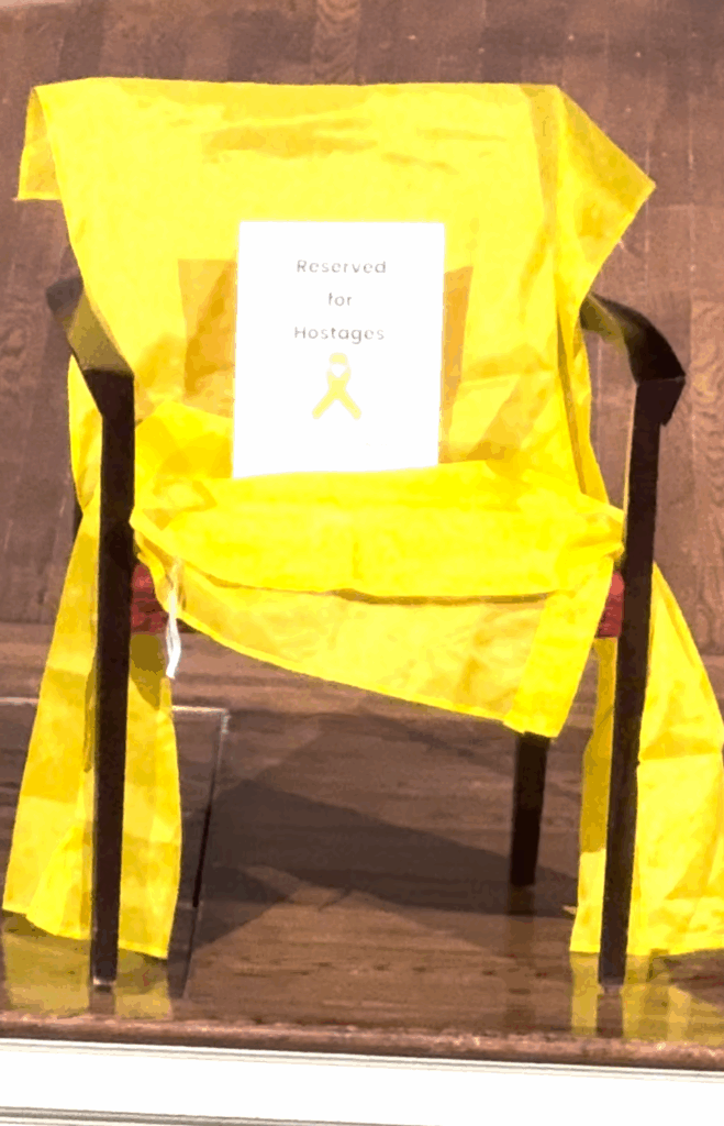 An empty chair draped in yellow cloth with a sign stating "reserved for hostages"