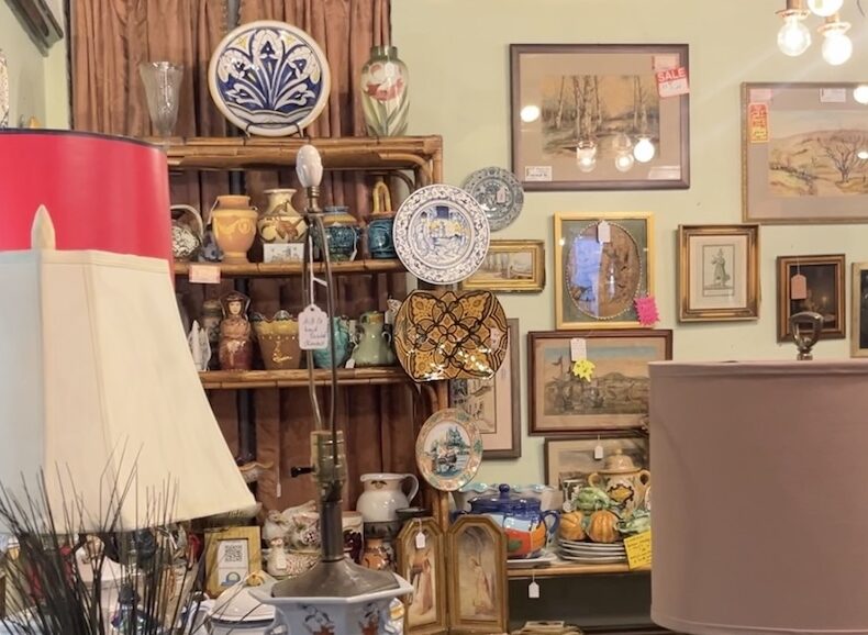 An antique dealer booth featuring colorful cermanic plates, dinnerware, and shade lamps.