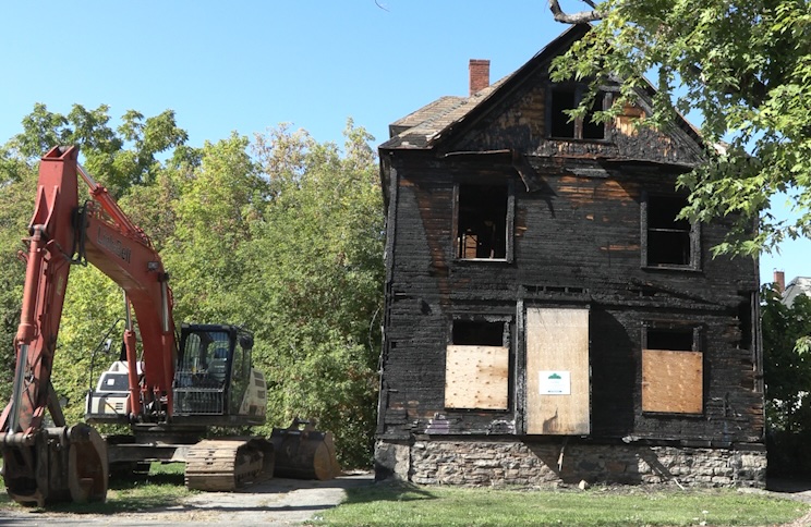 Charred remains of a vacant Southside Syracuse home. An excavator sits in what used to be the home's driveway.