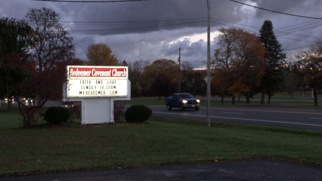 Redeemer Covenant Church's white sign welcomes drivers to the parking lot.