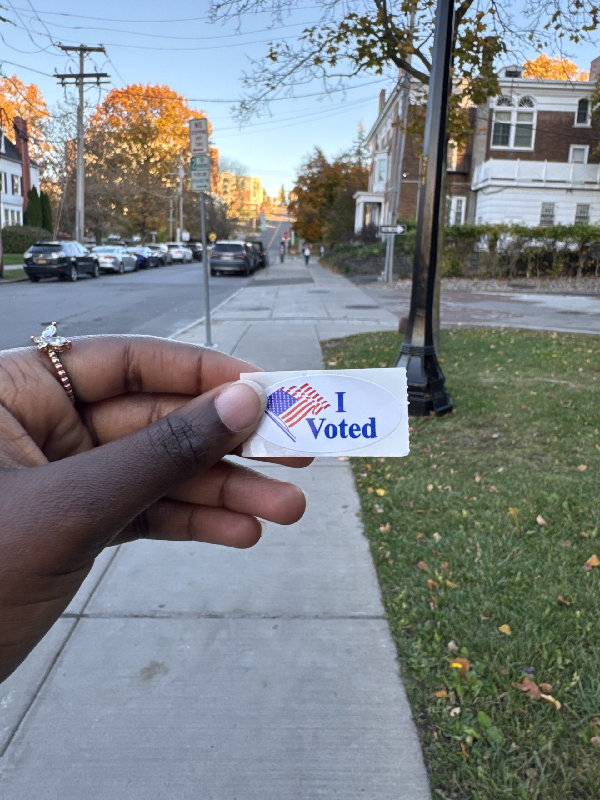 Sticker from polling center that says "I Voted" behind held up.