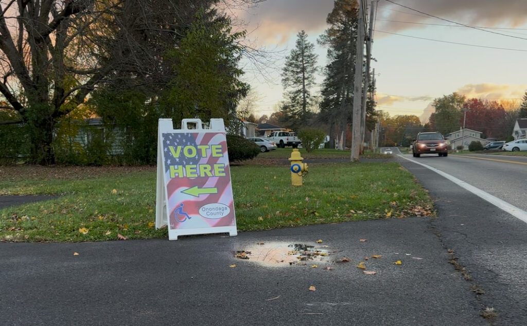A “Vote Here” sign with an American flag design sits beside a suburban road in Onondaga County, directing residents to a nearby polling place on Election Day.