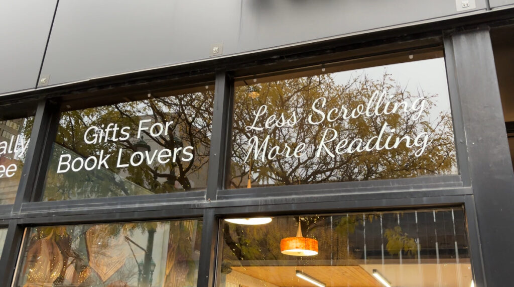 A sign on the glass outside of Parthenon Books that says "Less Scrolling More Reading"