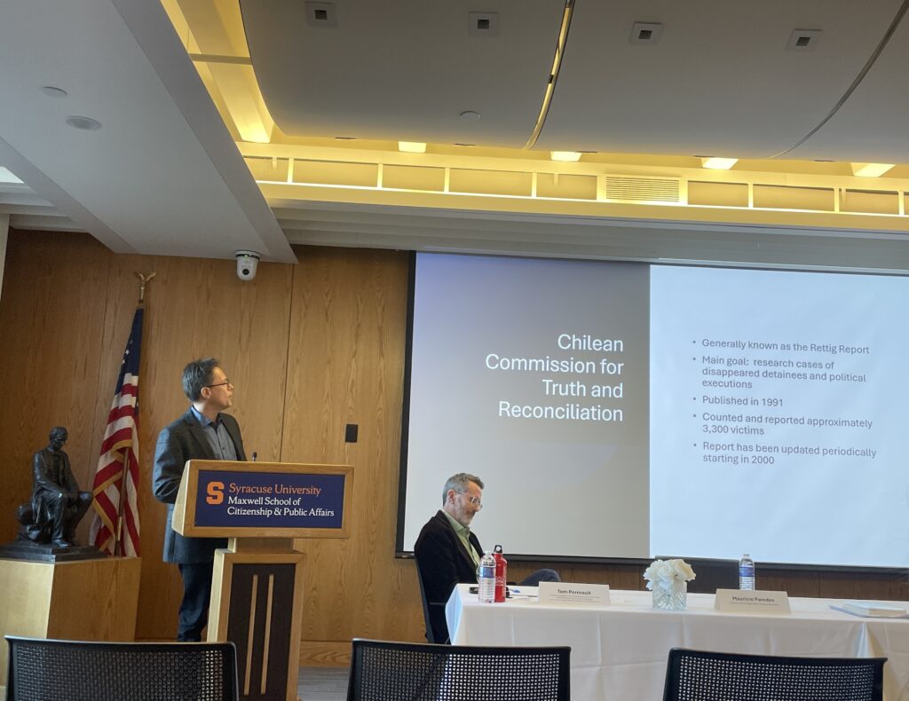 Paredes presents a slide at the panel discussion "Lessos from the South: Dictatorships and Resilience in Latin America." He is at a podium in the Strasser Legacy room in the Maxwell School.