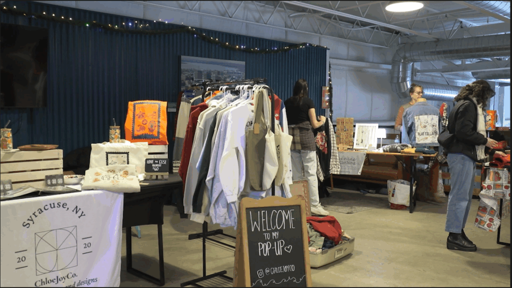 A pop up market at Harvey's Garden featuring clothes on a rack and a sign welcoming people to the pop up.