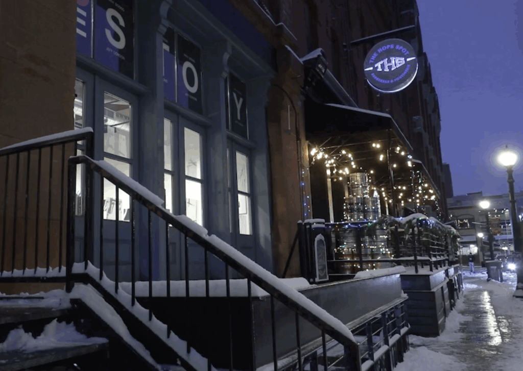 Exterior of ArtHaus Syracuse gallery at night, showing the entrance, snow-covered steps, and illuminated windows with art visible inside.