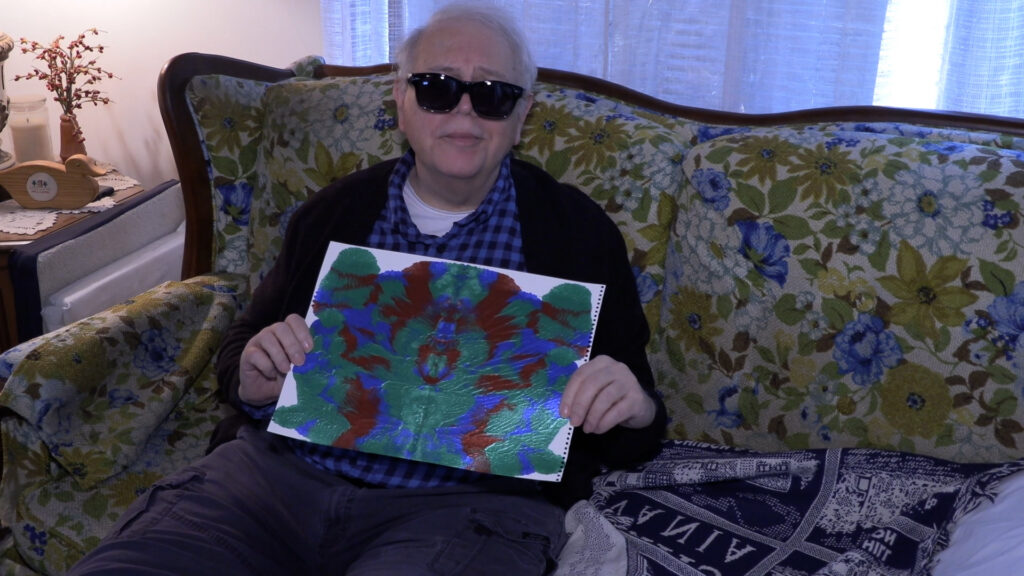 man sitting down holding up a painting