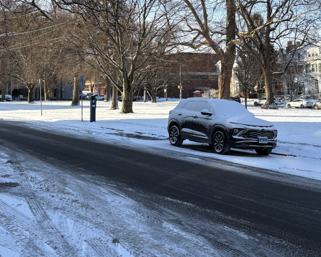 SUV covered in snow on a road with it's edges covered in ice and snow.
