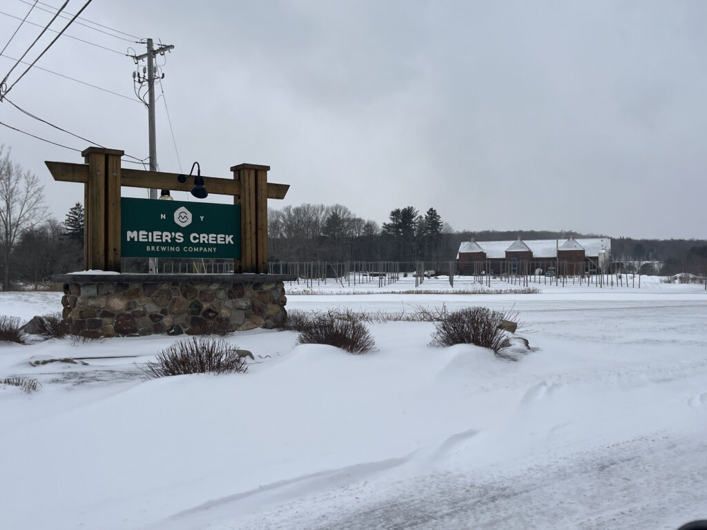 Green sign introducing the brewery on Ripperton road which is covered in snow.