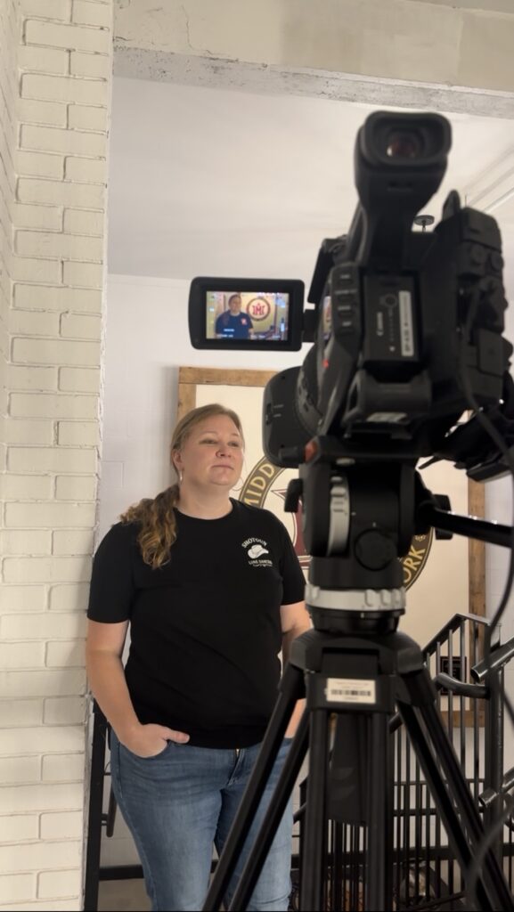 A woman stands in front of a video camera during an interview inside Middle Ages Brewery.