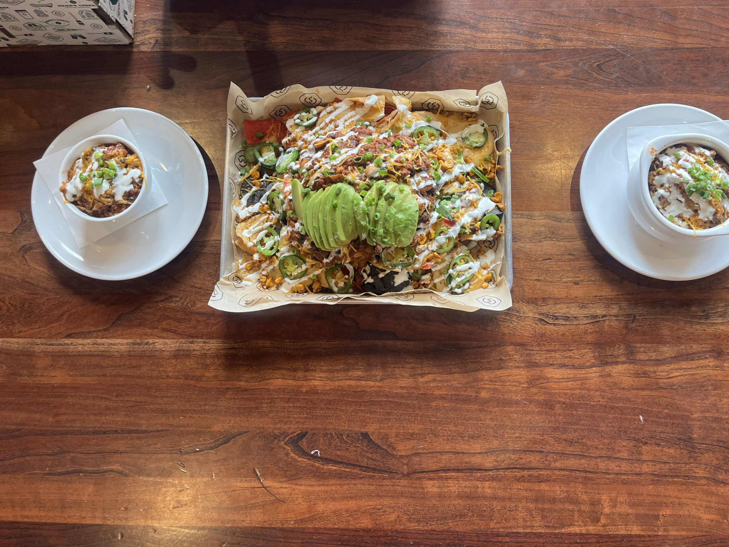 A cup of chili on the left, a rectangular chili cheese nacho plate in the middle, and a bowl of chili on the right.