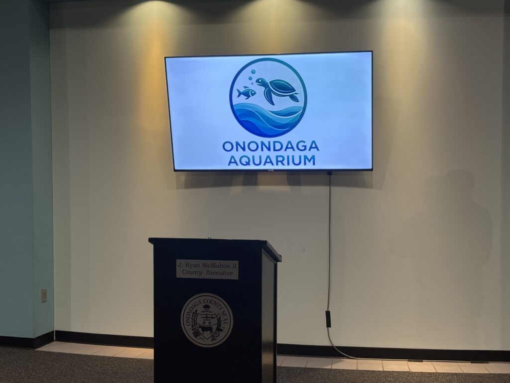 A television screen shows the Onondaga County Aquarium.
