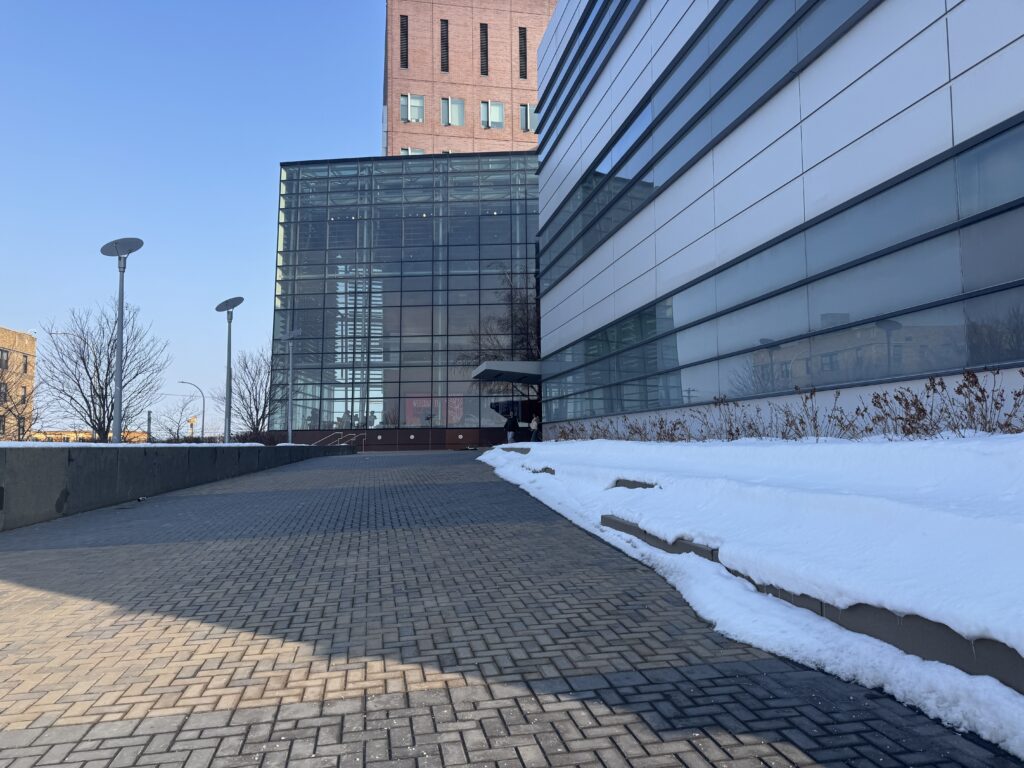 The Whitman School of Management building at Syracuse University has a clear pathway leading to the entrance and snow piled up along the side.