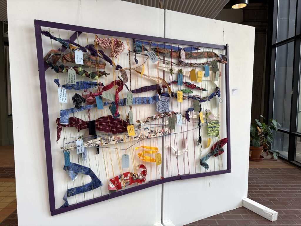A colorful display of ribbons and yarn attached to white wall.