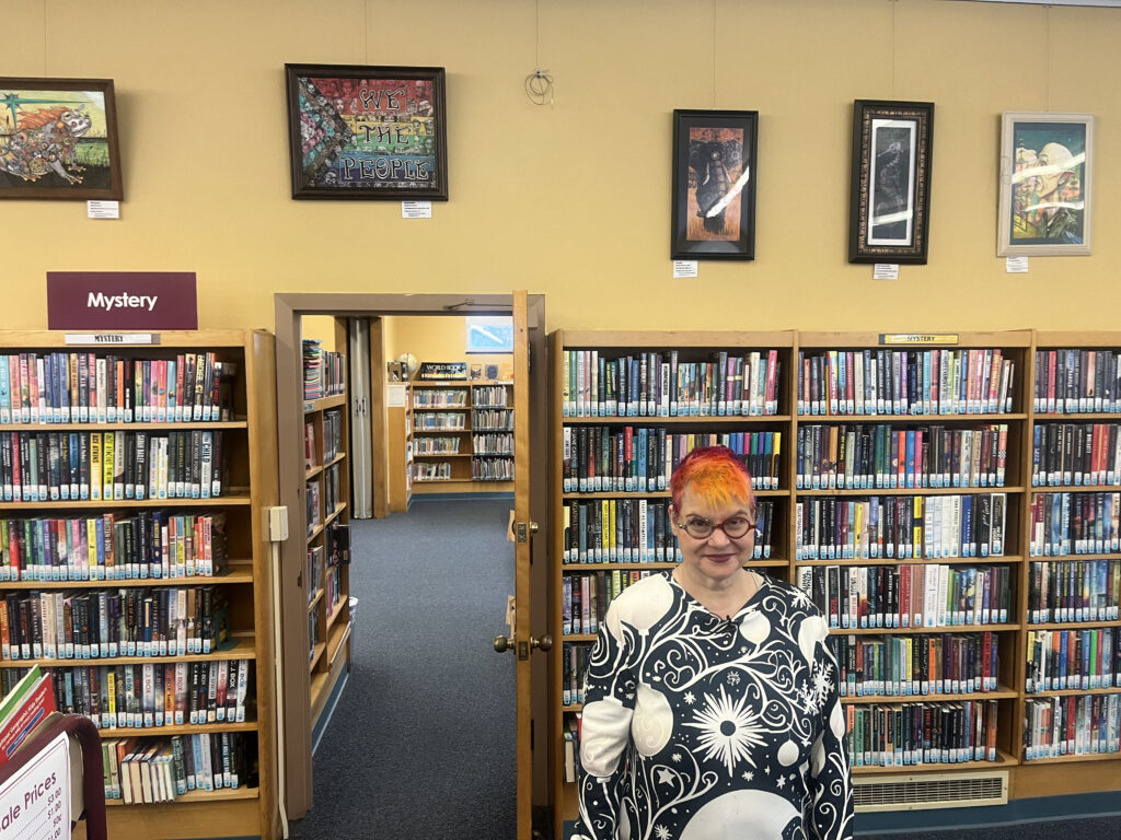 Syracuse artist Izzy Dugger dons her colorful hair in front of her work.