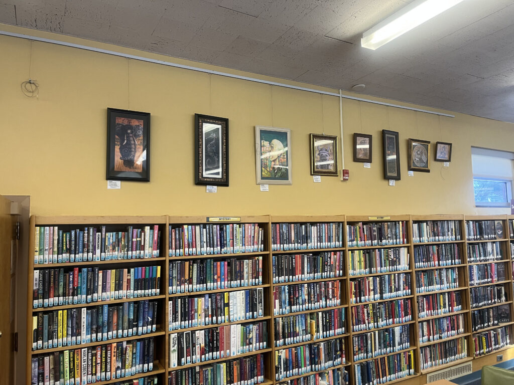 Art pieces hang high above book shelves at the library.