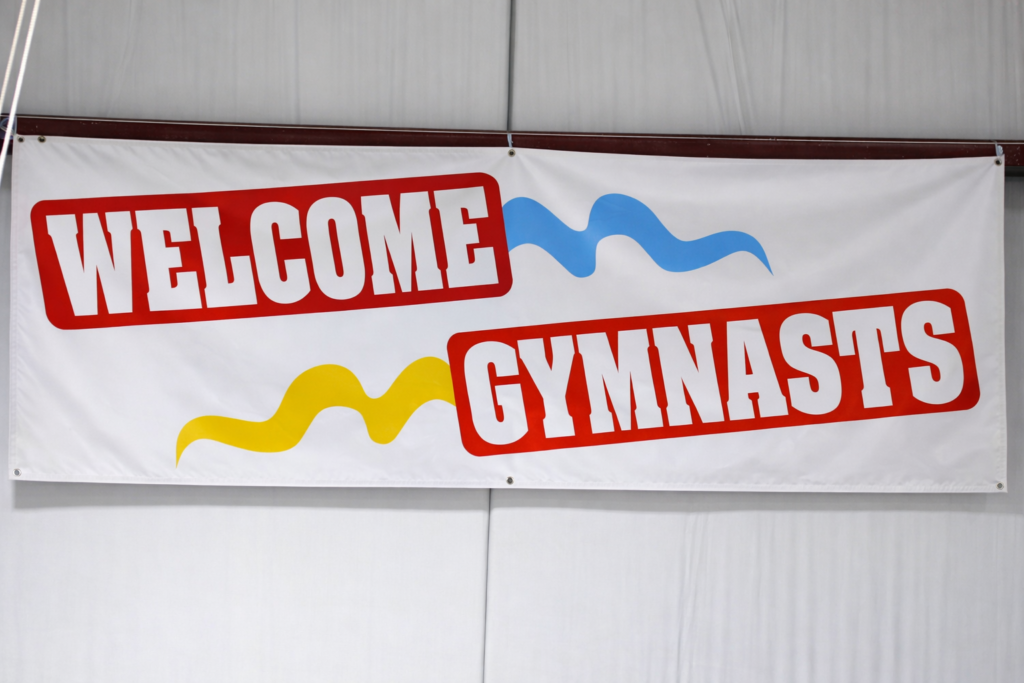 A banner reading “Welcome Gymnasts” hangs inside a gym facility.